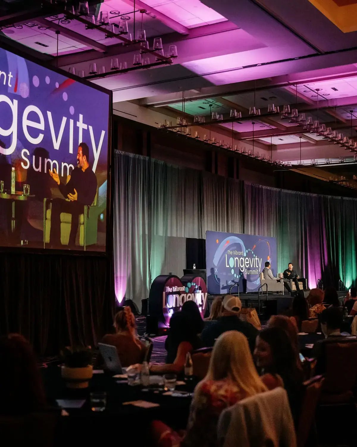 Vibrant Longevity Summit main stage, projection screens, speakers, and seated audience