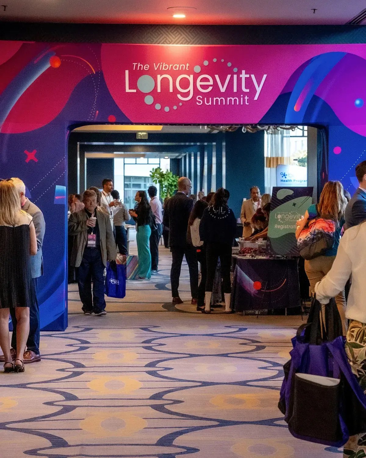 Busy conference registration area beneath the branded Vibrant Longevity Summit entrance